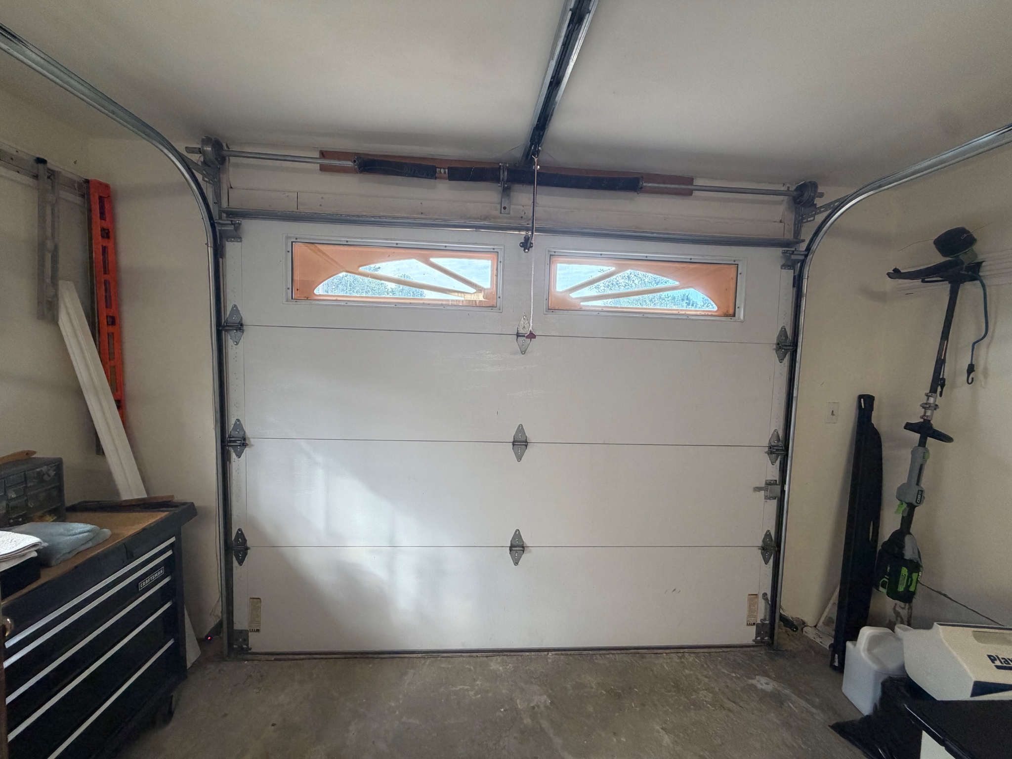 Inside a residential garage showing the sectional door, tracks, torsion springs and opener rail