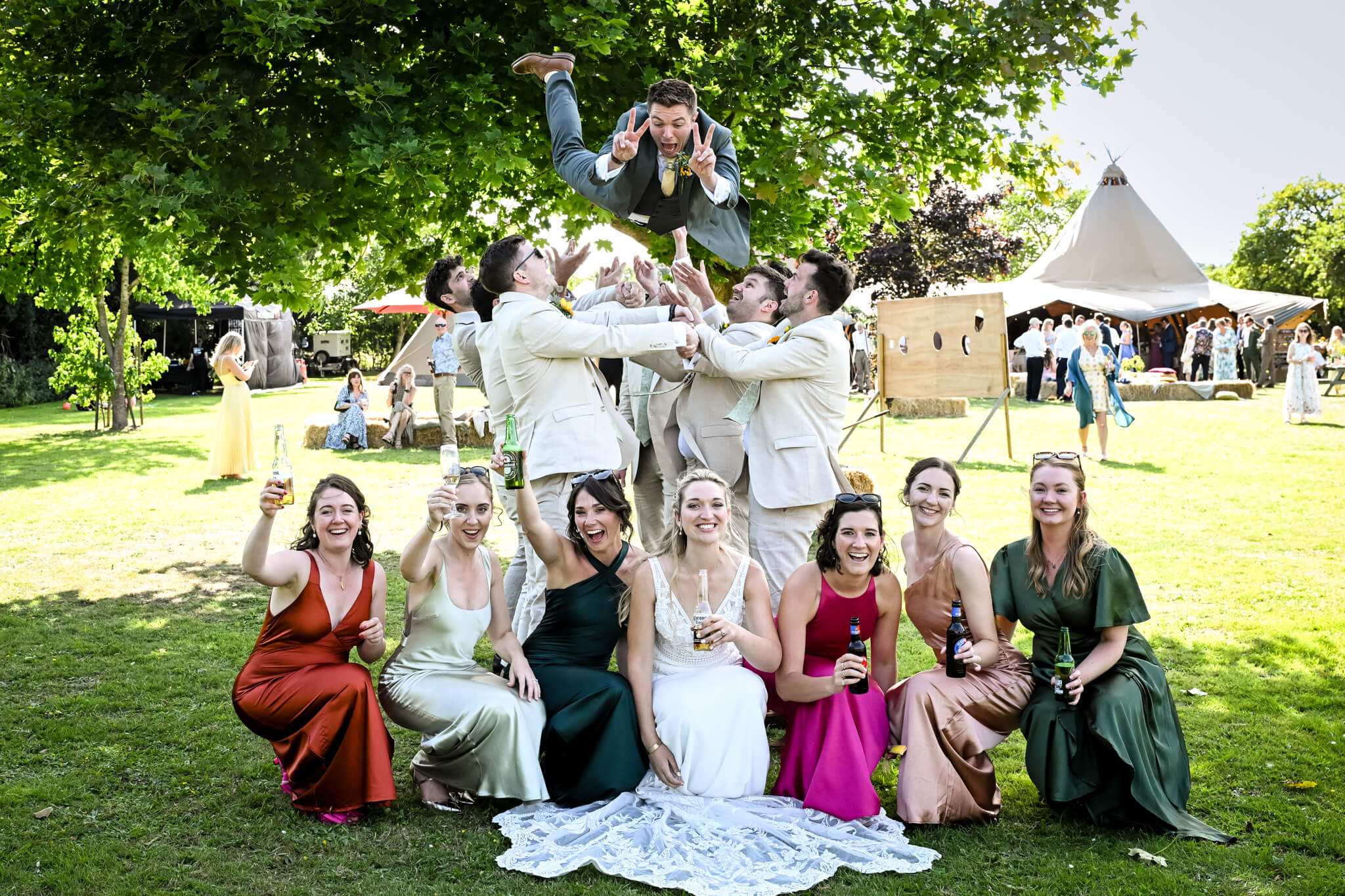 Groom flying through the air as bride and bridesmaid crouched down. Capture by relaxed sussex wedding photographer Paul Streeter-Staniford